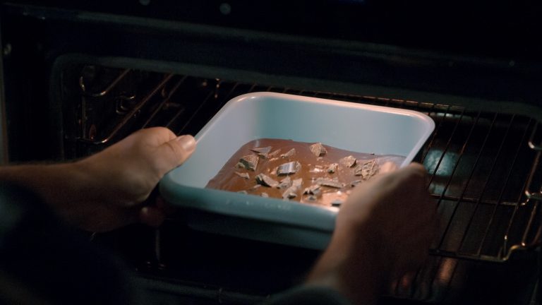 A baking pan full of melted chocolate being slid into a lit up oven